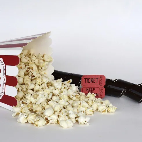 Eine offene Popcorntüte mit vielen Kernen, die ausgegossen sind. Daneben liegen Tickets und ein Filmstreifen.