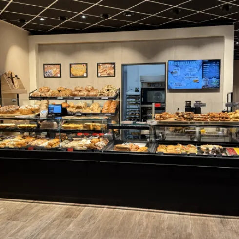 Ein modernes Café mit einer ansprechenden Auswahl an Backwaren und Süßigkeiten. Die Auslage ist gut beleuchtet und einladend.