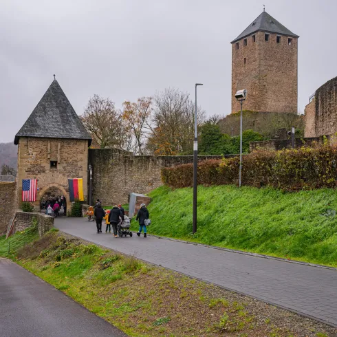 Ein historisches Schloss mit Türmen und einer Steinmauer. Besucher gehen den Weg entlang, um das Schloss zu erkunden.