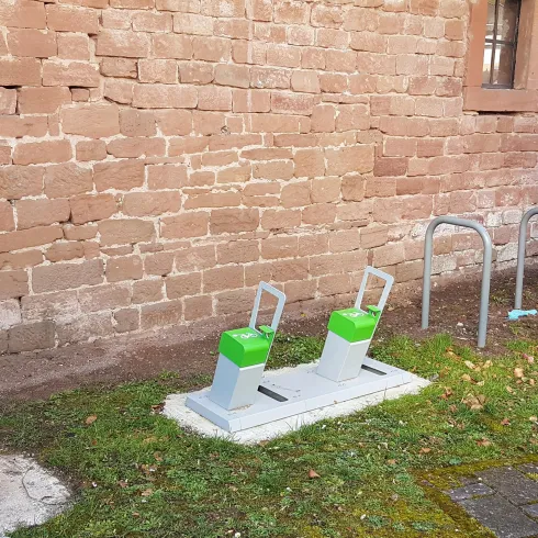 Ein Trainingsbereich im Freien mit Geräten zum Fitness. Es gibt auch einen Fahrradständer und eine Wand aus Stein im Hintergrund.