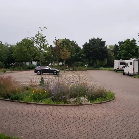 Ein ruhiger Stellplatz für Wohnmobile mit vereinzelten Fahrzeugen. Umgeben von Grünflächen und Bäumen.
