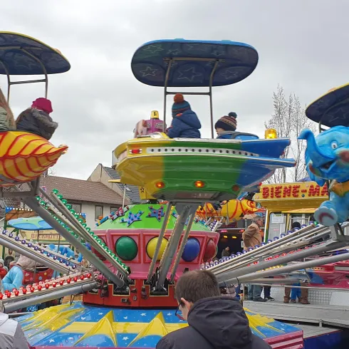 Ein bunter Karussell mit vielen Fahrgästen auf Fahrt. Menschen stehen um das Karussell herum und genießen die festliche Atmosphäre.
