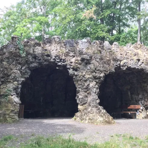 Eine einzigartige Steinhütte mit zwei Öffnungen, umgeben von Bäumen. Der Boden ist uneben und das Gelände ist grün.