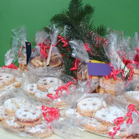 Eine Auswahl von festlich verpackten Keksen mit roten Schleifen. Im Hintergrund steht ein Tannenzweig, der eine weihnachtliche Stimmung verbreitet.