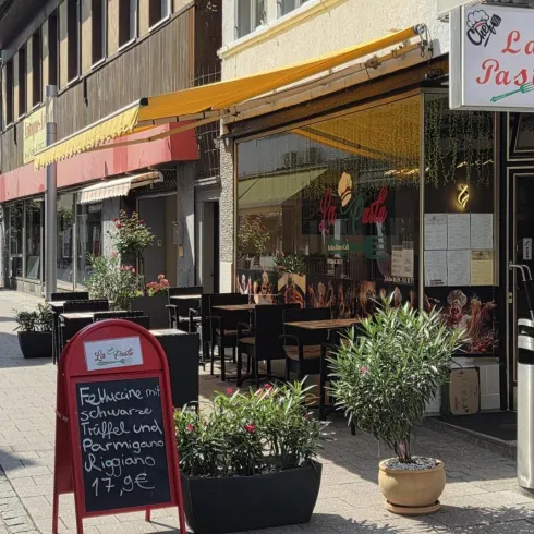 Ein italienisches Restaurant namens "La Pasta" mit einer einladenden Außenterrasse. Auf einem Schild werden spezielle Gerichte und Preise angezeigt.