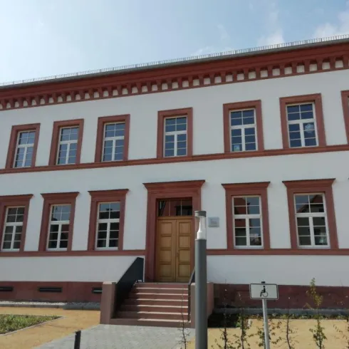 Ein modernes Gebäude mit einer weißen Fassade und roten Zierelementen. Es hat mehrere Fenster und einen Eingang mit Stufen.