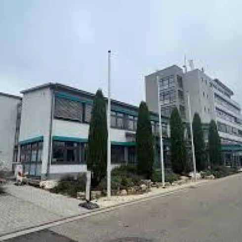 Ein modernes Bürogebäude mit mehreren Stockwerken und großen Fenstern. Im Vordergrund sind gepflegte Grünanlagen und ein Parkplatz zu sehen.