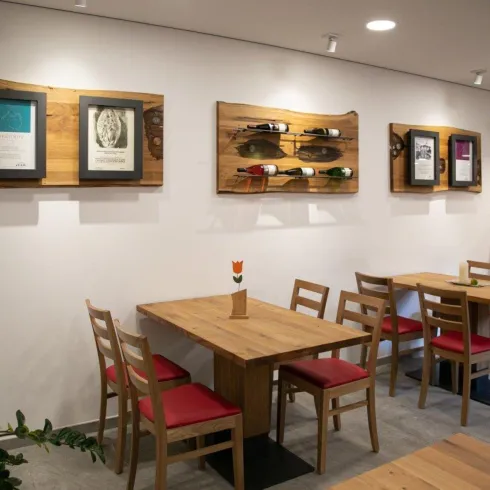 Ein gemütliches Restaurant mit Holztischen und roten Stühlen. An den Wänden hängen gerahmte Bilder und Weinfässer.