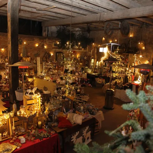 Ein festlich dekorierter Raum mit vielen leuchtenden Lichtern und handgefertigten Weihnachtswaren. Der Innenraum hat eine gemütliche Atmosphäre und erinnert an einen Weihnachtsmarkt.