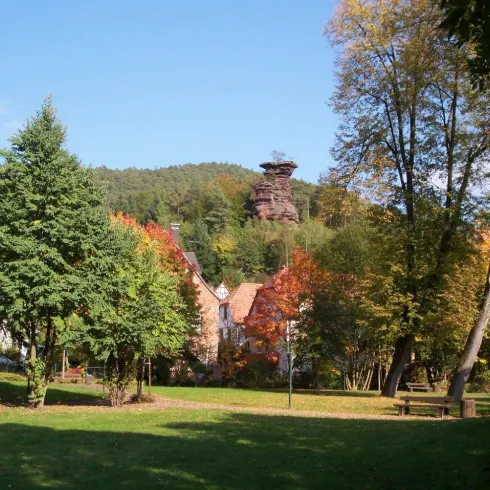 Eine malerische Landschaft mit bunten Herbstbäumen und einer kleinen Stadt im Vordergrund. Im Hintergrund ragt ein hoher Felsen hervor.