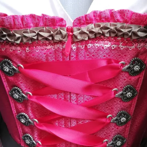 Ein traditionelles Dirndl in leuchtendem Pink mit versehenen Schnürungen. Es ist mit eleganten Details und einer passenden Bluse kombiniert.