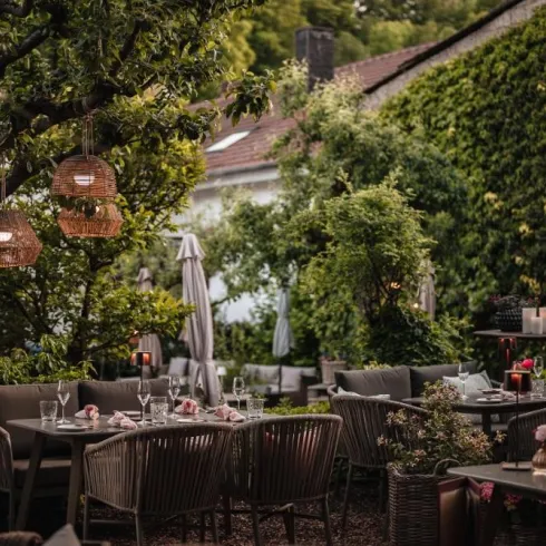 Ein charmantes Restaurant im Freien mit gepflückten Tischen und gemütlicher Atmosphäre. Grüne Pflanzen und stilvolle Beleuchtung schaffen eine einladende Umgebung.