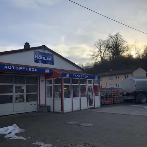 Ein Tankshop mit einem Bereich für Autopflege. Im Hintergrund sind Bäume und ein Lkw zu sehen.