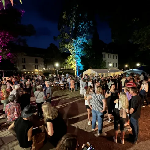 Eine lebendige Nachtveranstaltung mit vielen Menschen, die in einer festlichen Atmosphäre tanzen und feiern. Bunte Lichter und Zelte schaffen eine einladende Stimmung.