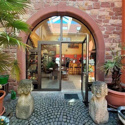 Ein einladender Eingang mit Glastür und runden Steinskulpturen auf beiden Seiten. Im Inneren sind Pflanzen und Möbel zu sehen, die eine gemütliche Atmosphäre schaffen.