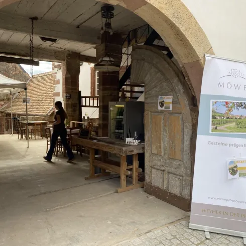Ein gemütlicher Innenhof eines Restaurants mit Holzstühlen und Tischen. An einer Wand steht ein Banner, das Weine bewirbt.