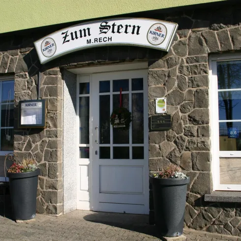 Ein traditionelles Gasthaus mit einem Steinfassade und weißen Fenstern. Über dem Eingang steht der Name "Zum Stern".
