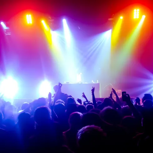 Eine Menschenmenge bei einem Live-Konzert mit bunten Lichtern. Der DJ steht auf der Bühne und sorgt für stimmungsvolle Musik.