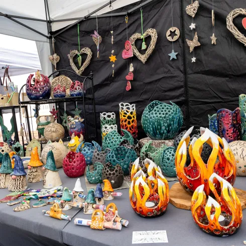 Ein Künstlermarkt mit einer Vielzahl von bunten, handgefertigten Töpferwaren und Dekorationen. Die Stände sind reich verziert mit Herzen, Sternen und farbenfrohen Keramiken.