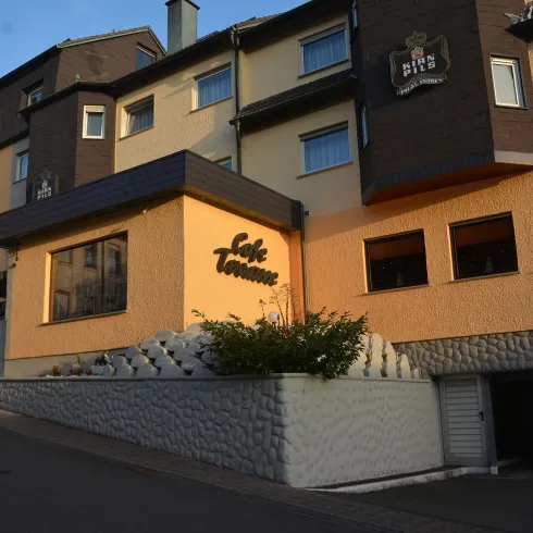 Ein modernes Gebäude mit einer hellen Fassade und großen Fenstern. Der Schriftzug „Cafe Terrasse“ ist deutlich sichtbar.