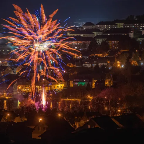 Ein spektakuläres Feuerwerk über einer Stadt bei Nacht. Die bunten Lichter reflektieren sich im Wasser und erhellen die Umgebung.