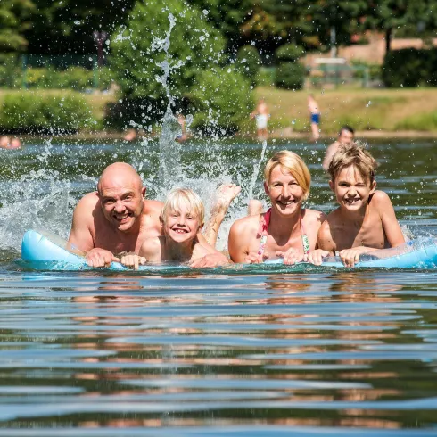 Eine Familie schwimmt auf einem Schwimmreifen im Wasser. Sie haben Spaß und spritzen mit Wasser.