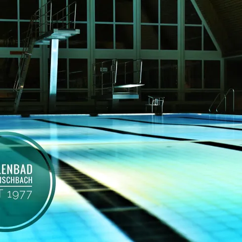 Ein Hallenbad mit klarem Wasser und einem Sprungbrett. Die Beleuchtung sorgt für eine angenehme Atmosphäre.