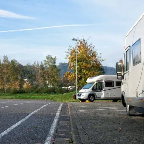 Zwei Wohnmobile parken am Straßenrand in einer ruhigen Umgebung. Im Hintergrund sind Bäume und ein malerisches Dorf zu sehen.