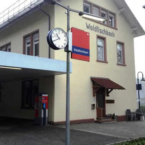 Ein Bahnhof mit dem Namen "Waldfischbach". Es gibt eine Uhr und einige Fenster an der Fassade des Gebäudes.