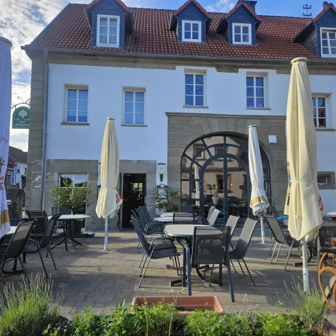 Ein Restaurant mit einer einladenden Terrasse und Sonnenschirmen. Das Gebäude hat eine helle Fassade und große Fenster.