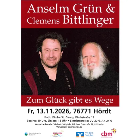 Ein Mann spielt Gitarre und singt in einem Raum mit bunten Fenstern. Es ist eine gemütliche Atmosphäre mit einem Tisch auf der linken Seite.