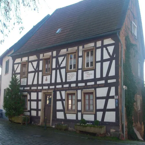 Ein historisches Fachwerkhaus mit einer gut erhaltenen Fassade. Es steht an einer ruhigen Straße, umgeben von kleinen Pflanzen.