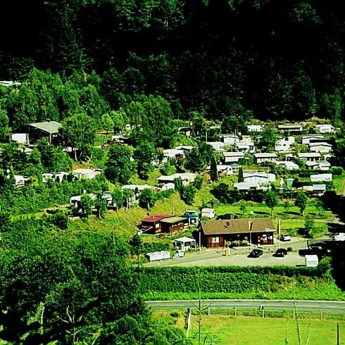Eine ruhige Campingplatzansicht umgeben von grünen Wäldern. Die Anlage besteht aus mehreren Wohnmobilen und einem Hauptgebäude.