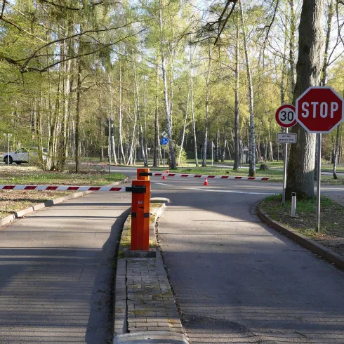 Ein Zugang zu einem Park mit einer Stoppschild und einer roten Feuerhydranten. Die Straße ist von Bäumen gesäumt und es gibt ein Absperrgitter.