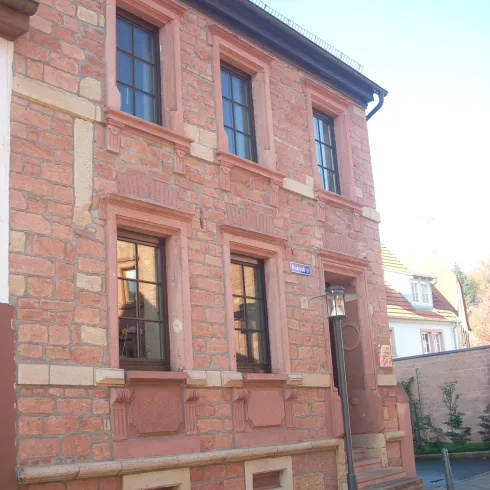 Ein rotes Steingebäude mit großen Fenstern und einem Eingang. Die Fassade zeigt klare architektonische Linien und eine einladende Atmosphäre.