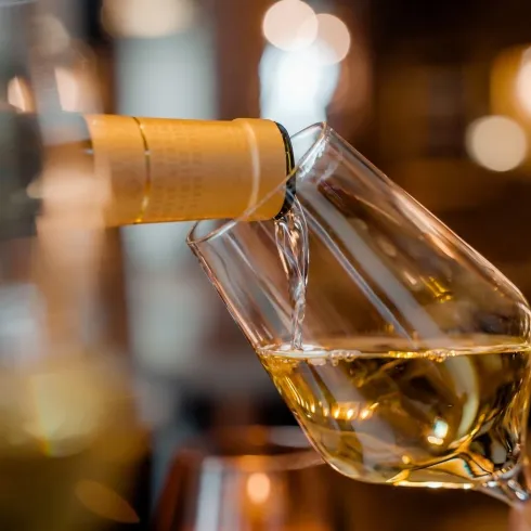 Ein Glas Wein wird aus einer Flasche eingegossen. Die Flüssigkeit hat eine goldene Farbe und wird in einem elegant gestalteten Glas serviert.