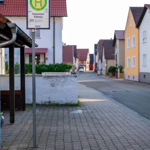 Eine ruhige Straße mit Wohnhäusern und einem Busbahnhofsschild. Die Umgebung ist sauber und gut gestaltet.