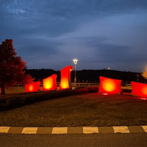 Eine künstlerische Landschaftsinstallation mit leuchtend roten Elementen. Die Umgebung ist abendlich beleuchtet und bietet eine ruhige Atmosphäre.