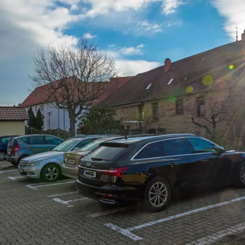 Ein Parkplatz mit mehreren Autos. Im Hintergrund sind Häuser und ein blauer Himmel zu sehen.