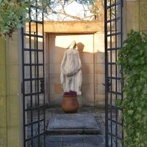 Ein hübscher Garten mit einer Statue im Hintergrund. Die Statue steht in einem Raum, der von einem schmiedeeisernen Tor umgeben ist.