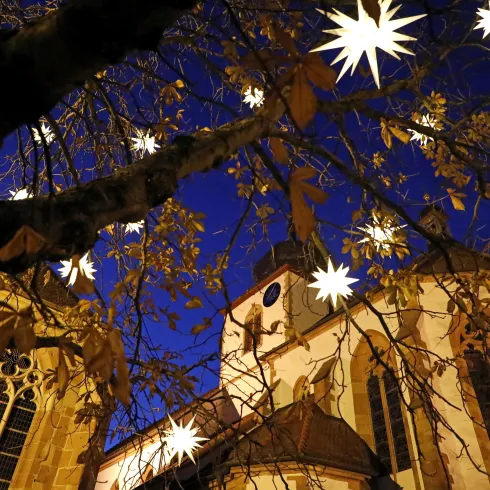Ein schöner Baum mit leuchtenden Sternen hängt vor einer Kirche bei Nacht. Der Himmel ist klar und dunkelblau.