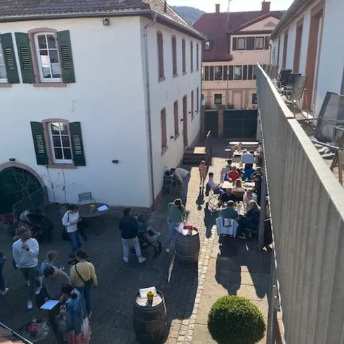 Ein belebter Innenhof mit Menschen, die sich versammeln und gemeinsam Zeit verbringen. Die Umgebung ist hell und einladend, mit Tischen und Stühlen unter freiem Himmel.