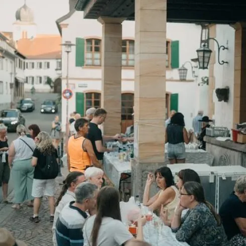 Eine belebte Freiluft-Gastronomie mit vielen Gästen. Es gibt Tische und Stühle, und die Atmosphäre ist gesellig und entspannt.