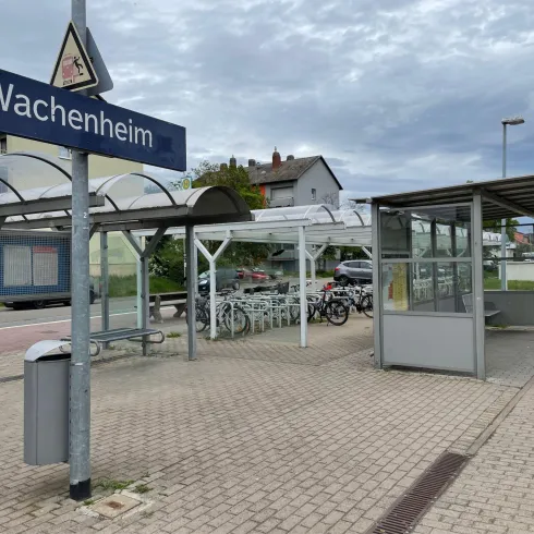 Eine Bushaltestelle in Wachenheim mit Wartebereich und Fahrradstellplätzen. Der Himmel ist bewölkt und die Umgebung ist städtisch.