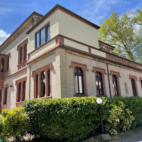 Ein schönes historisches Gebäude mit einer gut gepflegten Fassade. Umgeben von grünen Sträuchern und Bäumen strahlt es Charme und Eleganz aus.