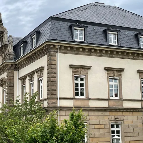 Ein historisches Gebäude mit schönen architektonischen Details. Es ist von Bäumen und einem grauen Himmel umgeben.