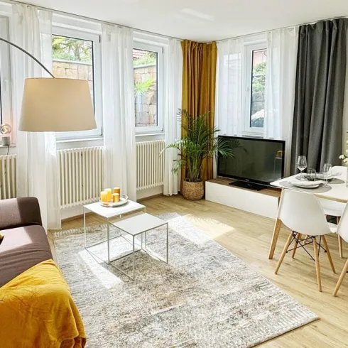 Geräumiges Wohnzimmer mit modernem Design und einer gemütlichen Couch. Ein Essbereich mit Tisch und Stühlen vervollständigt den Raum.