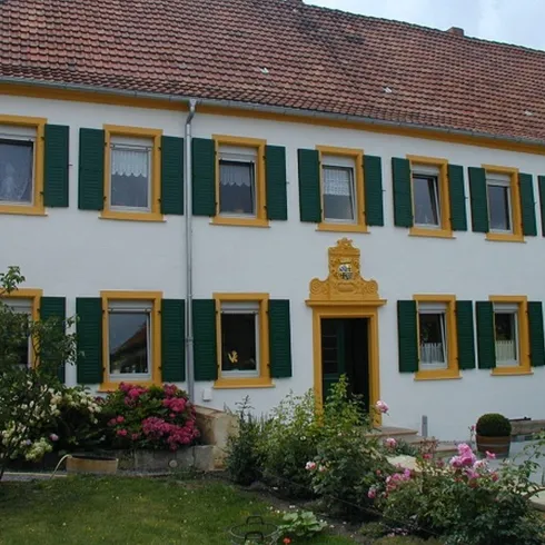 Ein schönes Haus mit gelben Fensterläden und einem roten Dach. Der Garten ist blühend mit verschiedenen Blumen.
