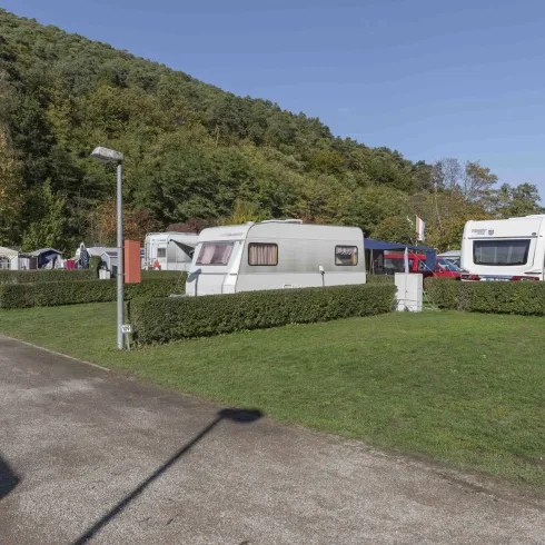 Ein Campingplatz mit mehreren Wohnwagen und Rasenflächen. Im Hintergrund ist ein bewaldeter Hang zu sehen.