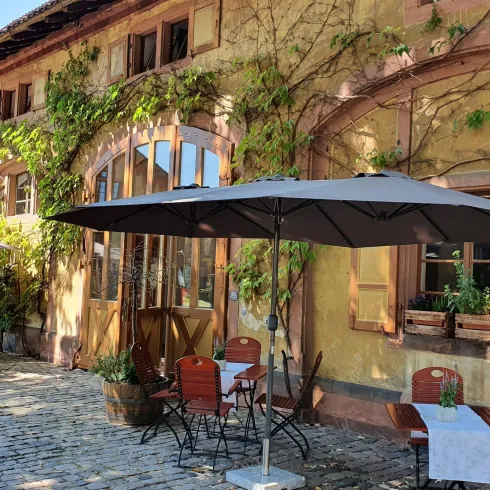 Eine charmante Restaurantterrasse mit sonnigen Schirmen und Tischen. Die Fassade ist mit Efeu bewachsen und vermittelt eine einladende Atmosphäre.